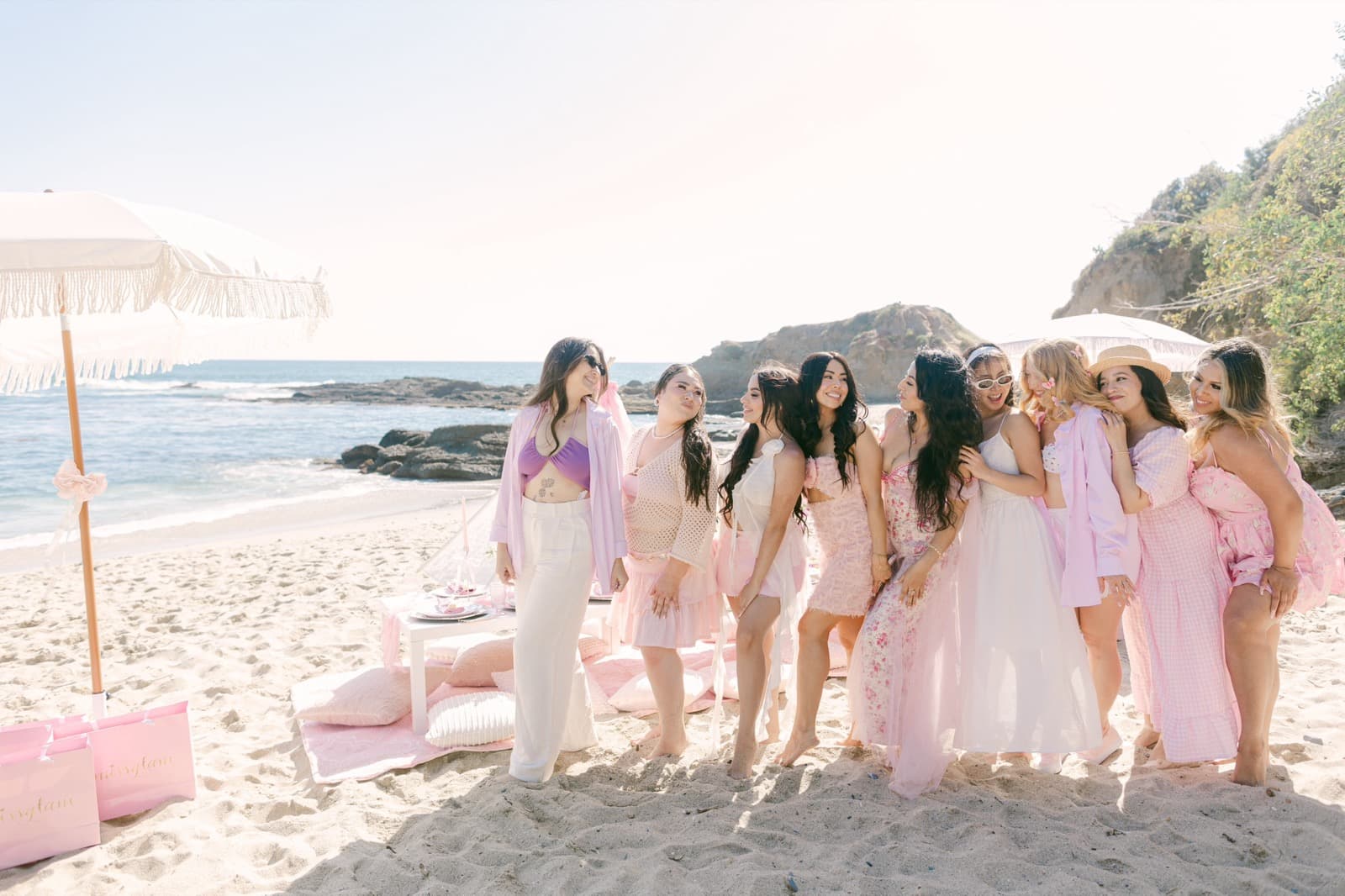 Guests in soft pinks gathered on a sunlit beach beside a styled Pixxie picnic