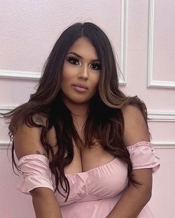 Gina, the founder of Pixxie Picnics, in a soft pink off-shoulder dress against a blush panelled wall, looking to camera