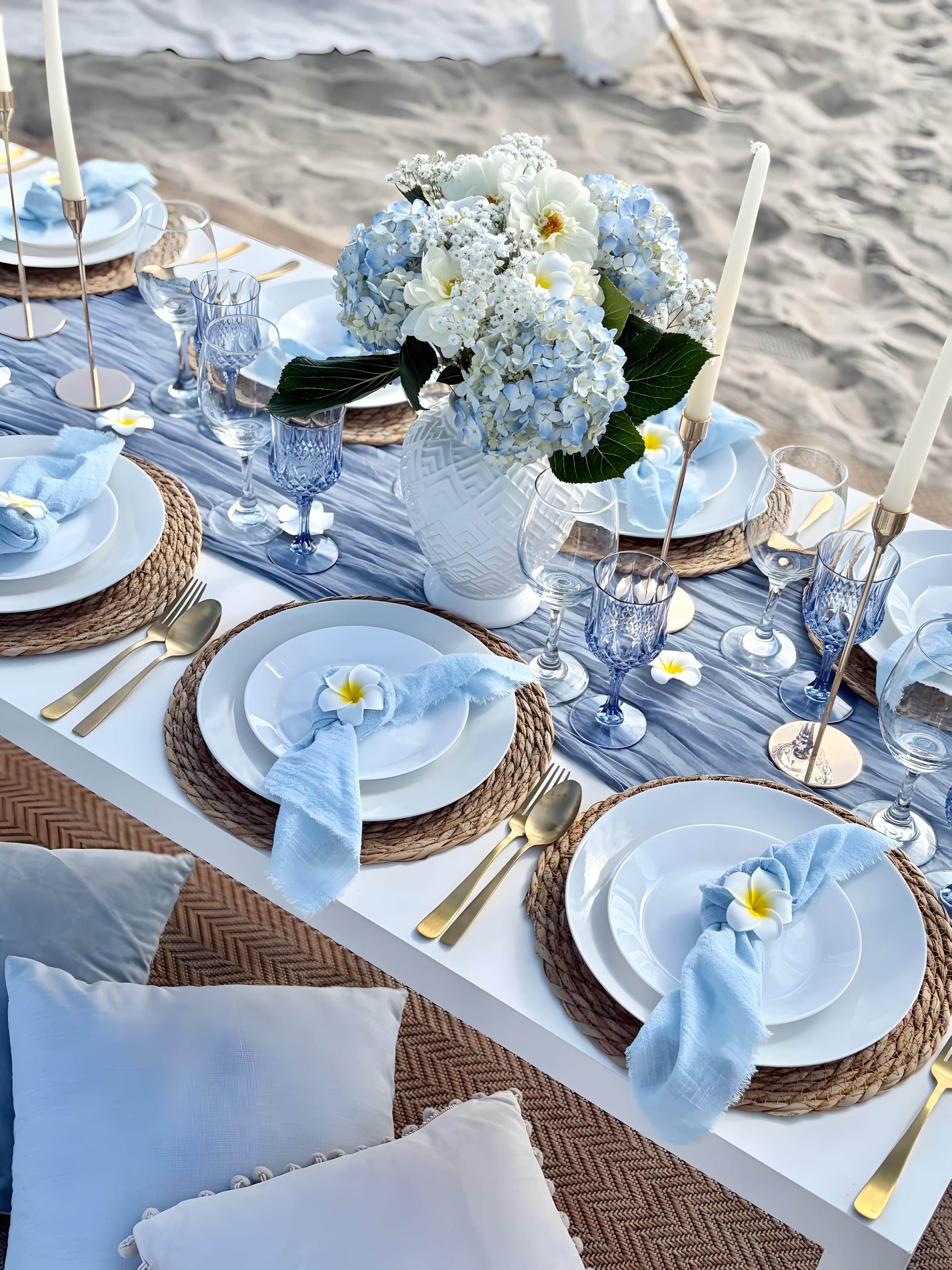 A dusty-blue beach place setting with white plates on jute chargers, blue gauze napkins and hydrangeas