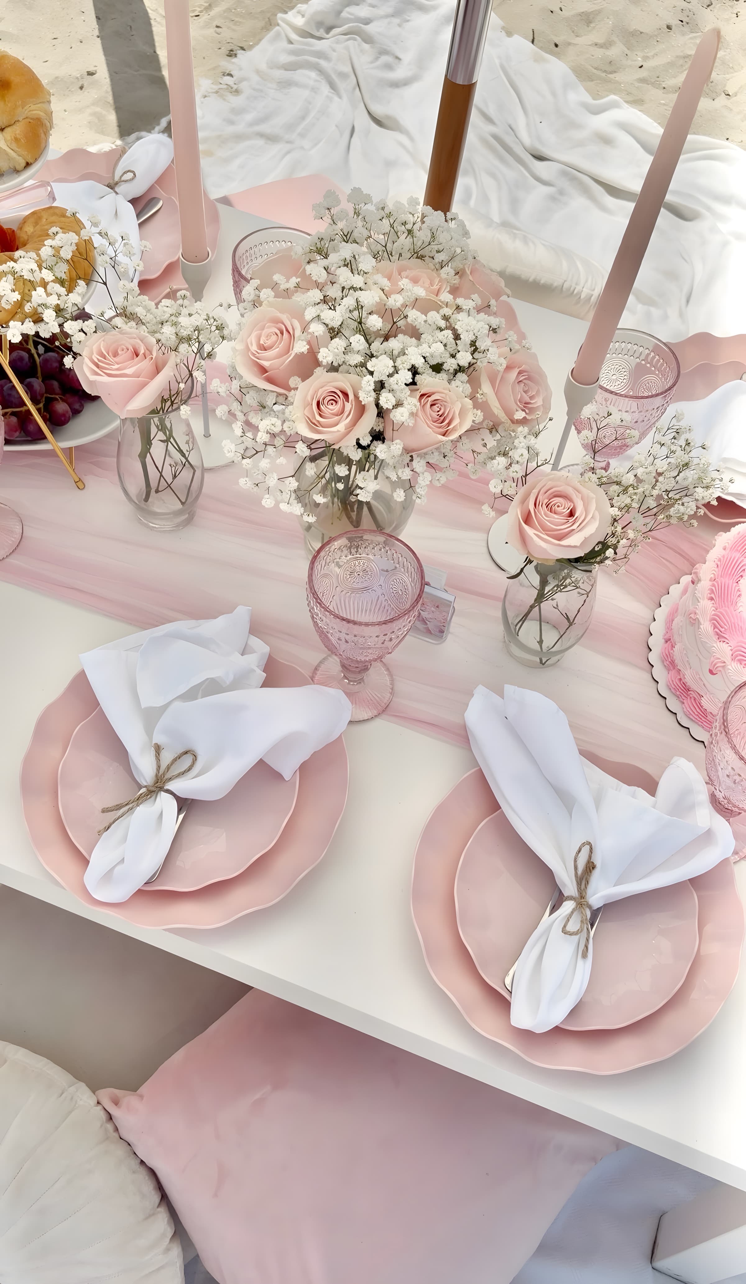 A blush place setting with pink scalloped plates, twine-bow napkins, pink goblets and a blush rose bouquet