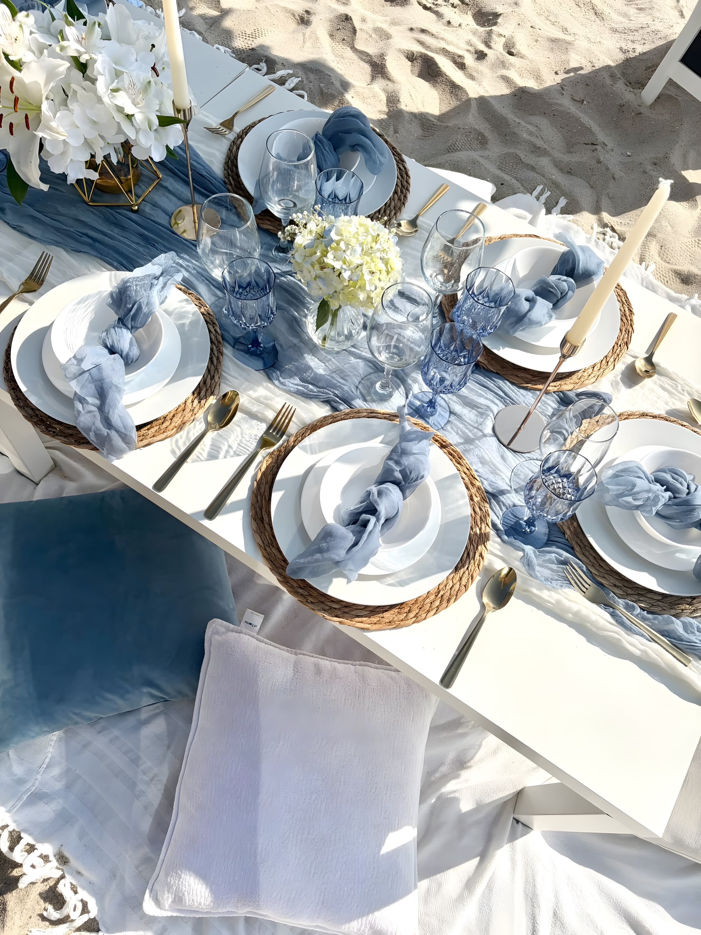 An overhead dusty-blue beach tablescape with white china, knotted blue napkins and white hydrangea