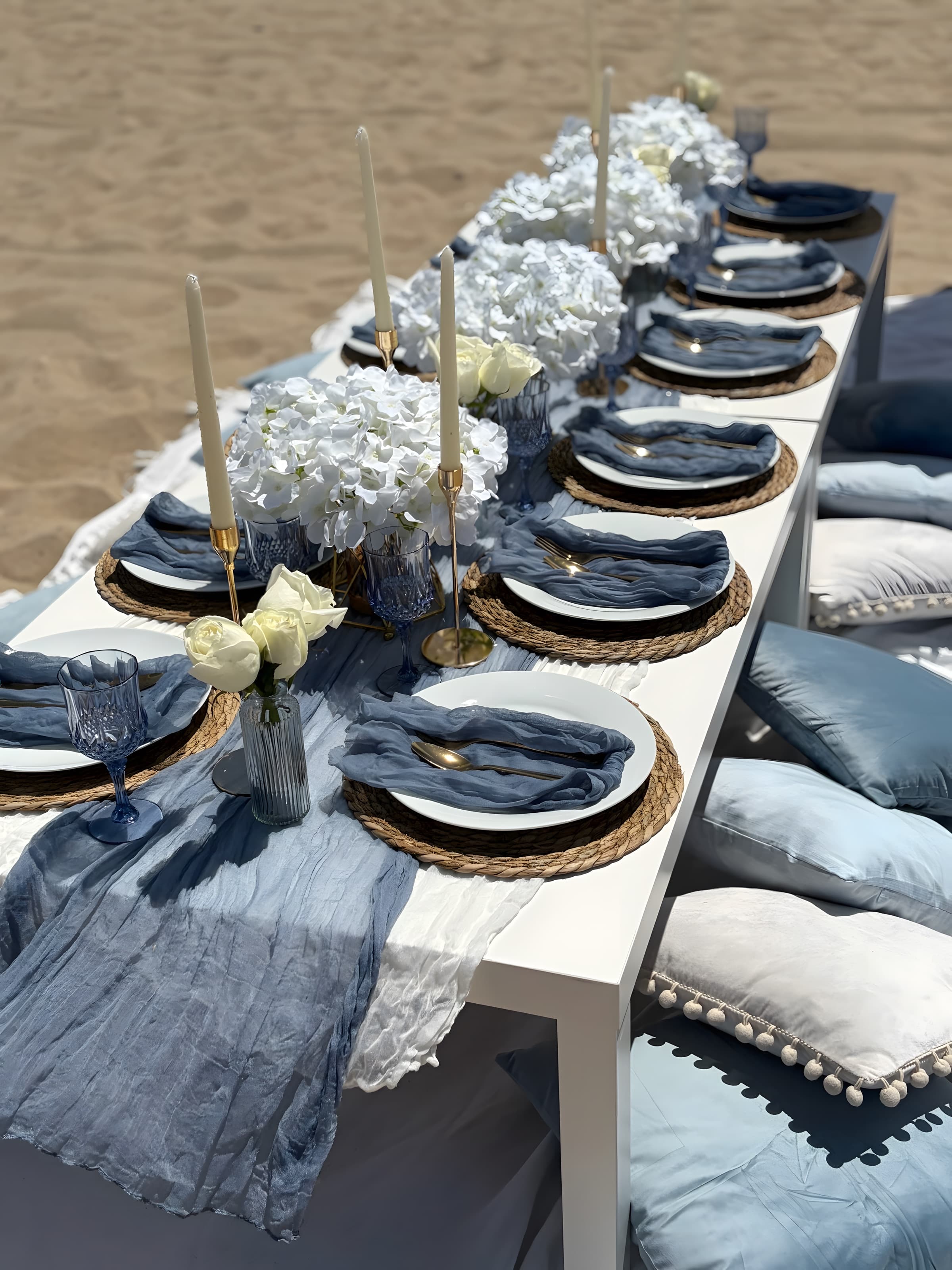 A tight dusty-blue place setting with white plates on woven chargers, blue napkins and blue goblets