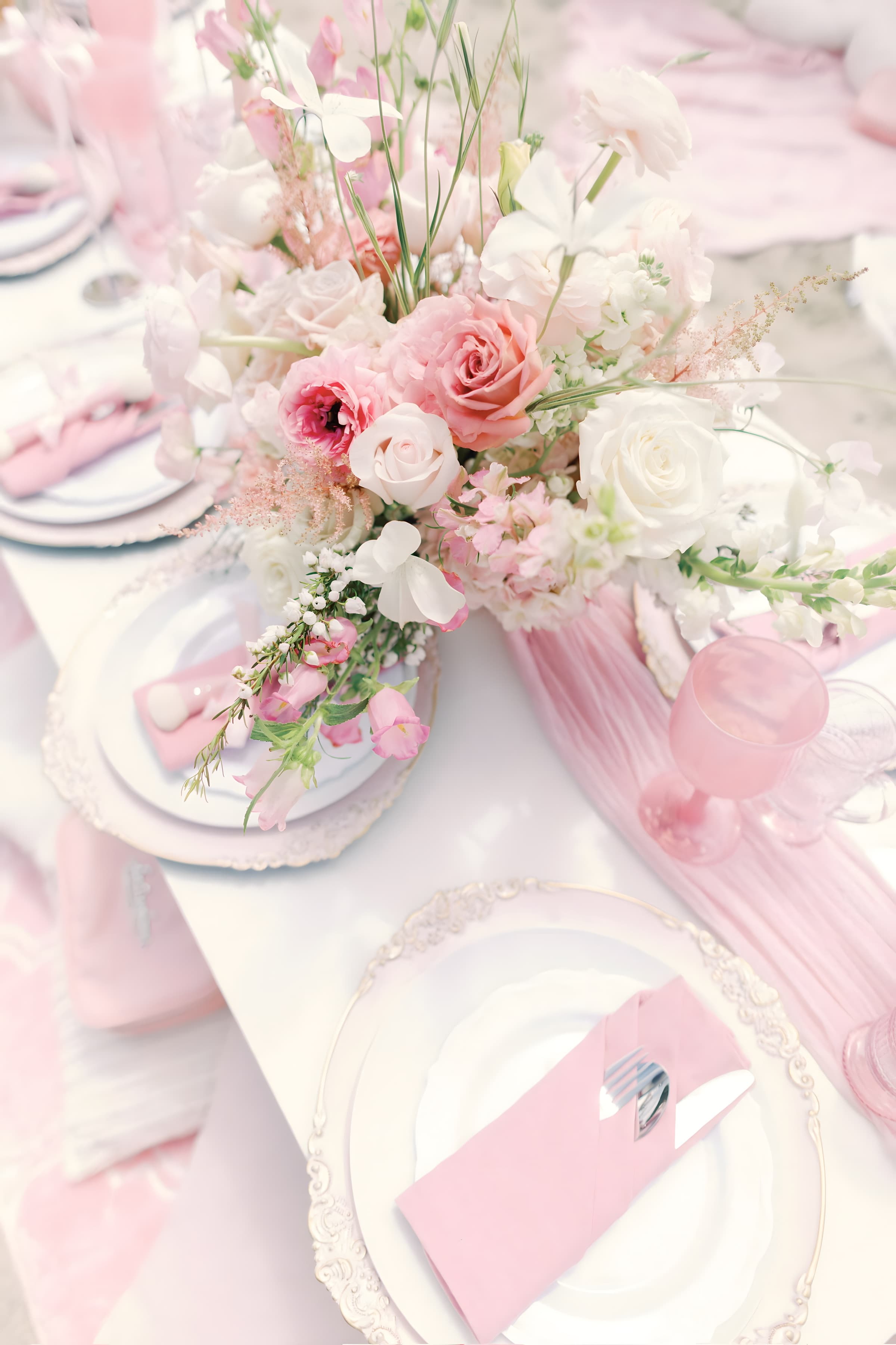 An elevated wide of a full pink cove table with abundant blush florals and a lace teepee, ocean horizon
