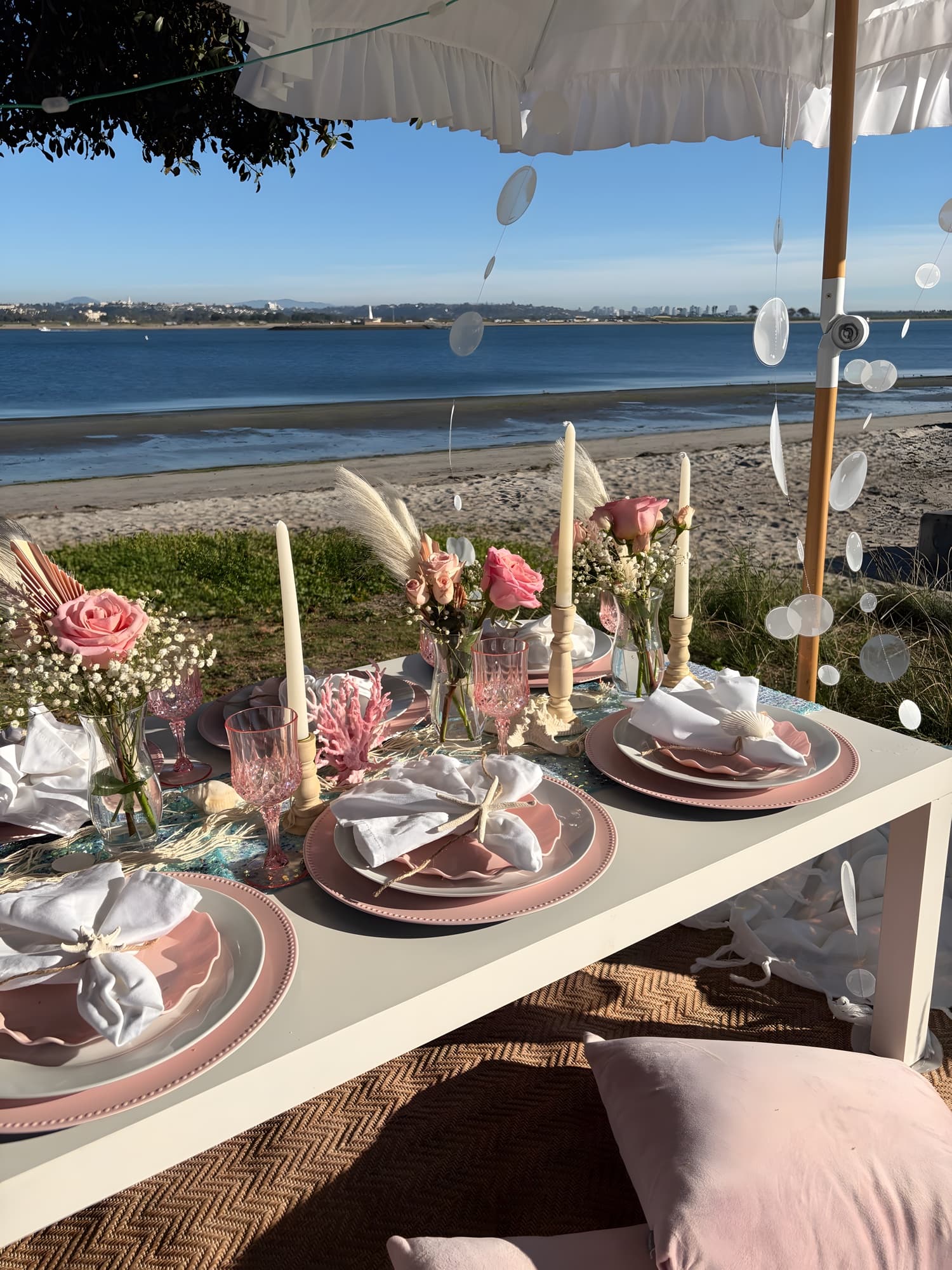 A pink “under the sea” beach table with scalloped plates, coral accents and pink roses, the San Diego bay behind
